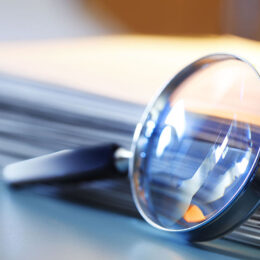 A magnifying glass leans against a thick stack of papers. Photographed with a very shallow depth of field.